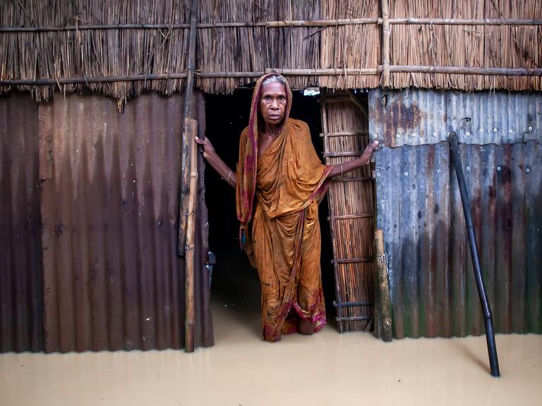 Eine ältere Frau steht am 6. Oktober 2024 vor ihrem Haus im knietiefen Hochwasser in einem Dorf im Jhenaigati Upazila des Bezirks Sherpur in Bangladesch. 