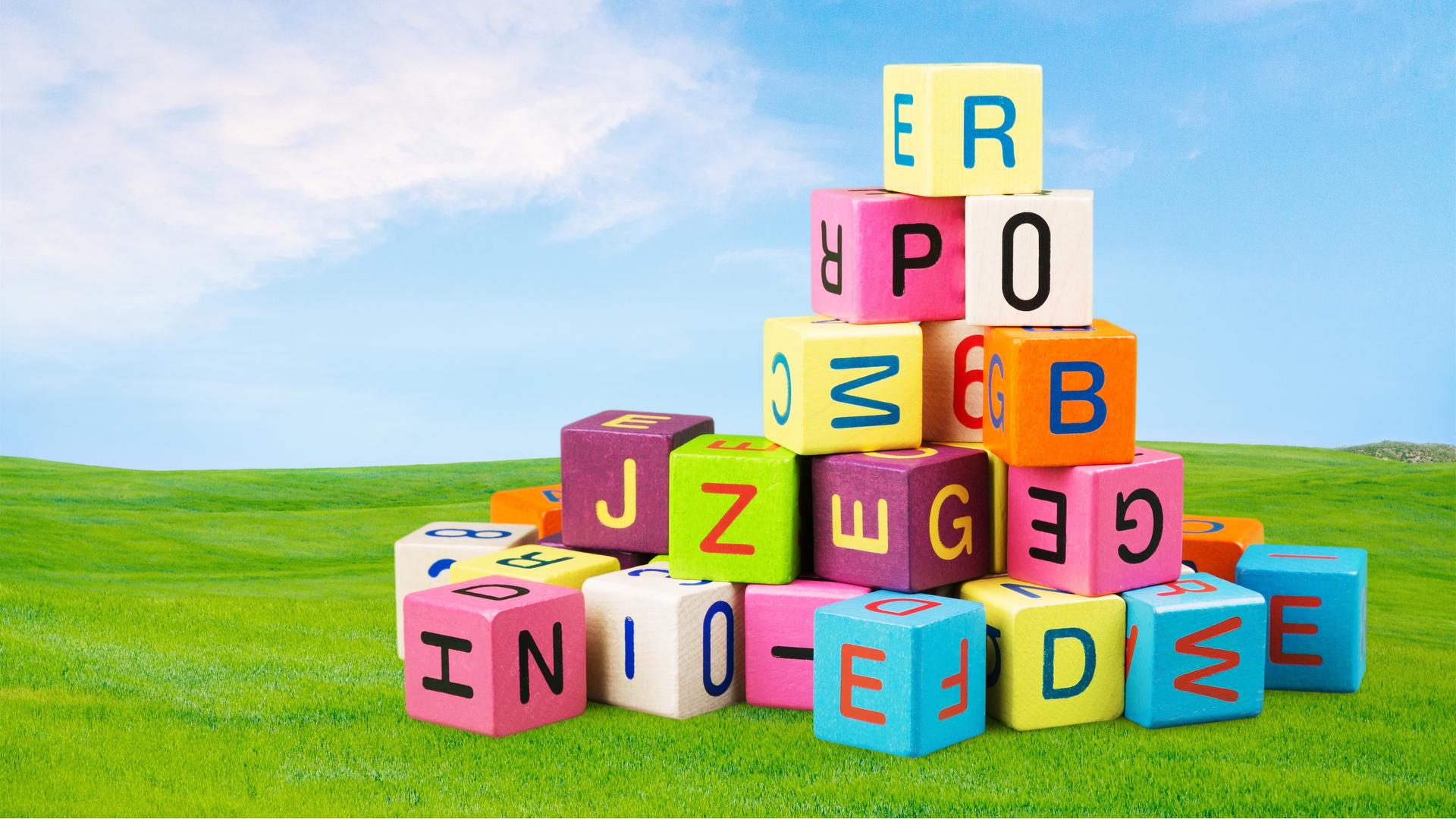 Buchstabenklötze bunt auf einem Haufen vor einem Landschaftshintergrund