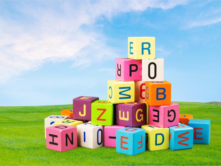 Buchstabenklötze bunt auf einem Haufen vor einem Landschaftshintergrund