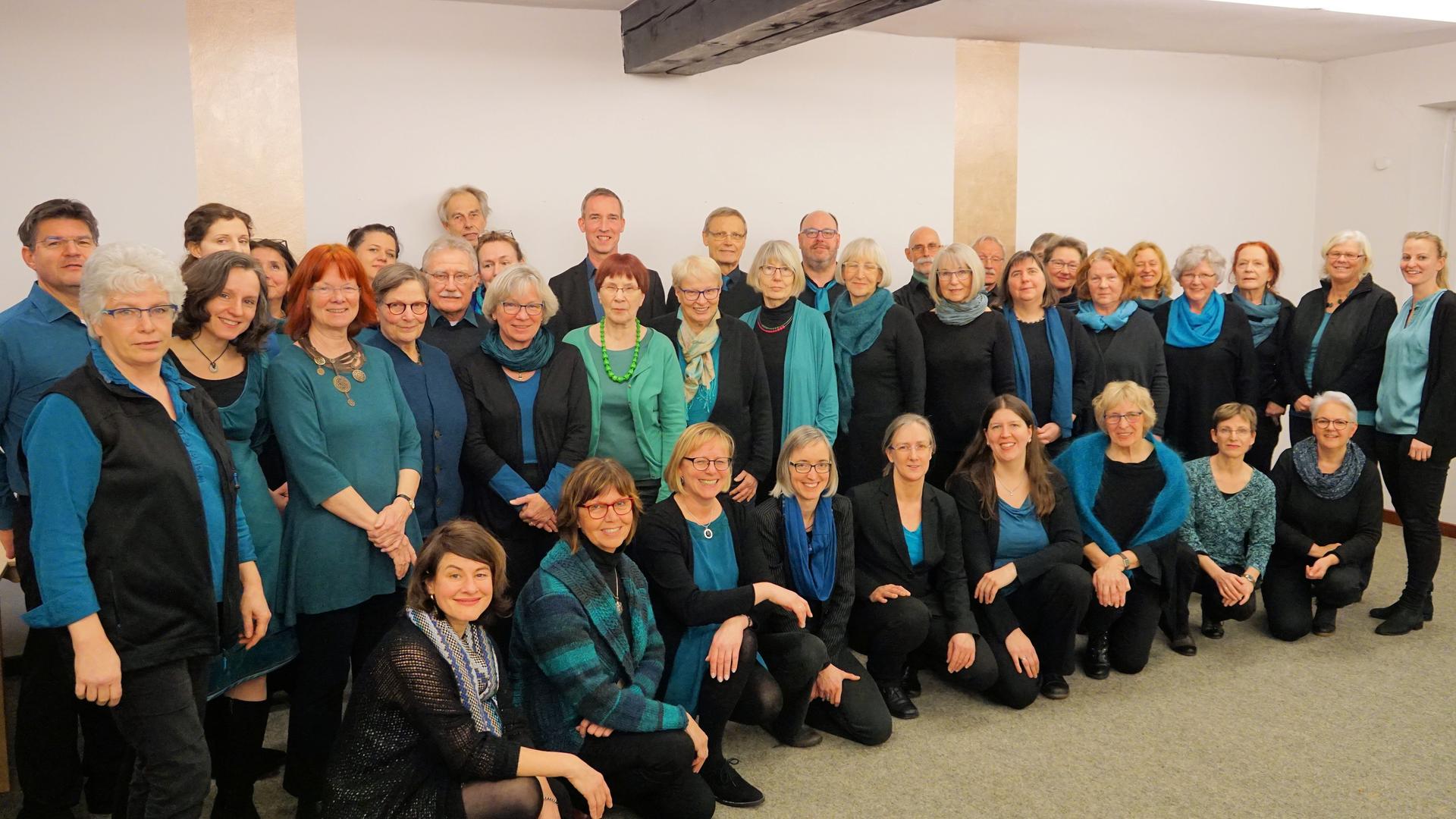 Gruppenbild der Sängerinnen und Sänger in schwarzer Kleidung mit blauen oder türkisen Oberteilen