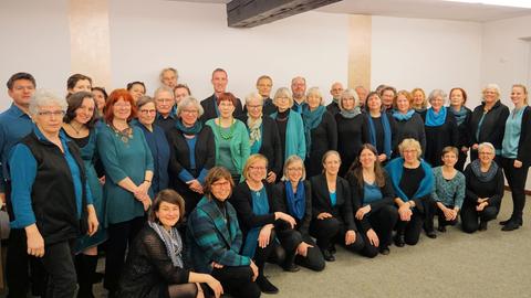 Gruppenbild der Sängerinnen und Sänger in schwarzer Kleidung mit blauen oder türkisen Oberteilen
