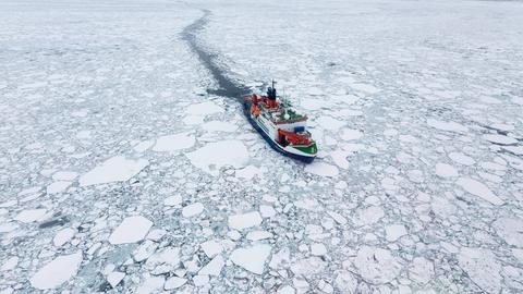 Das Forschungsschiff Polarstern fährt im arktischen Meer an großen Eisschollen vorbei.