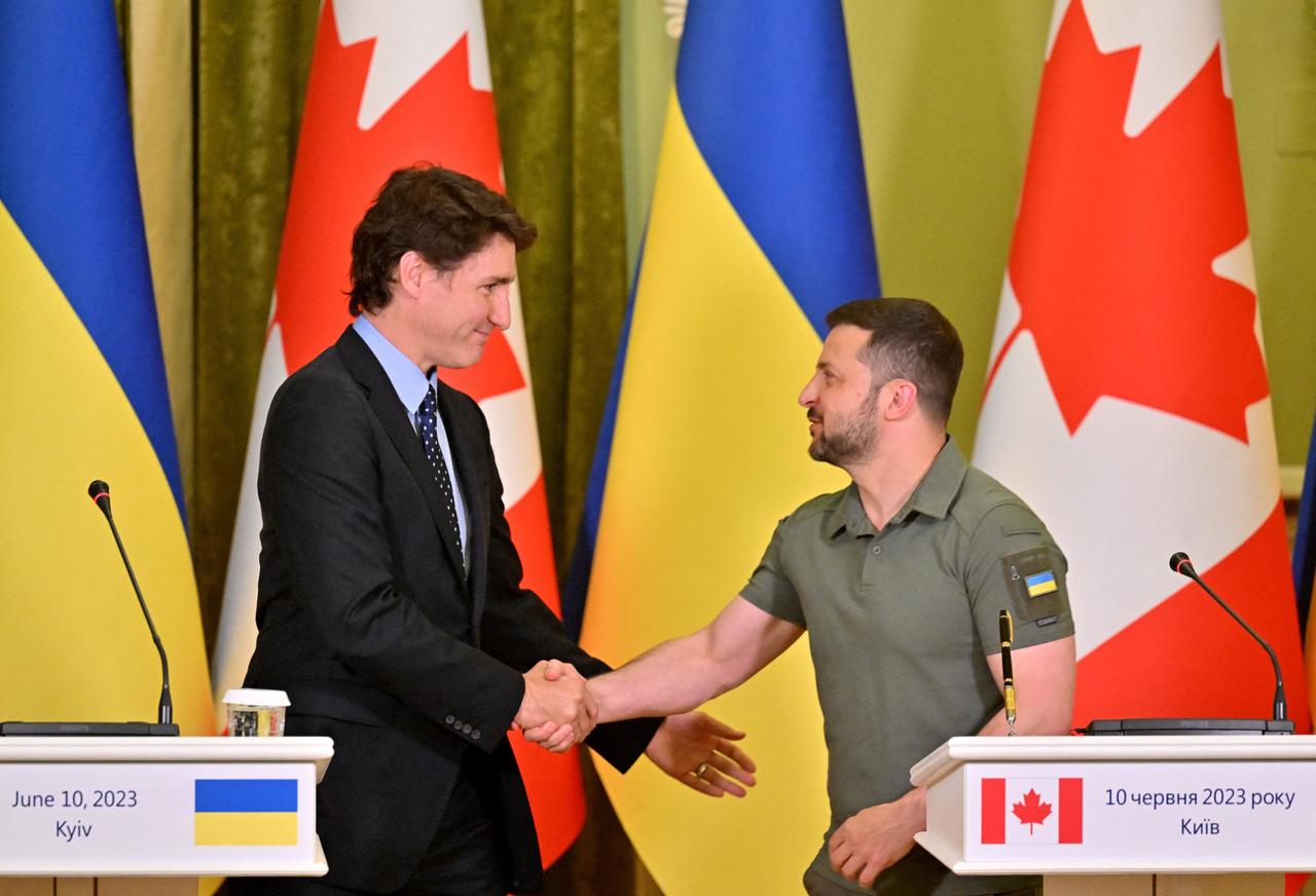 Trudeau und Selenskyj auf einem Podium vor ihren Landesflaggen geben sich die Hand.