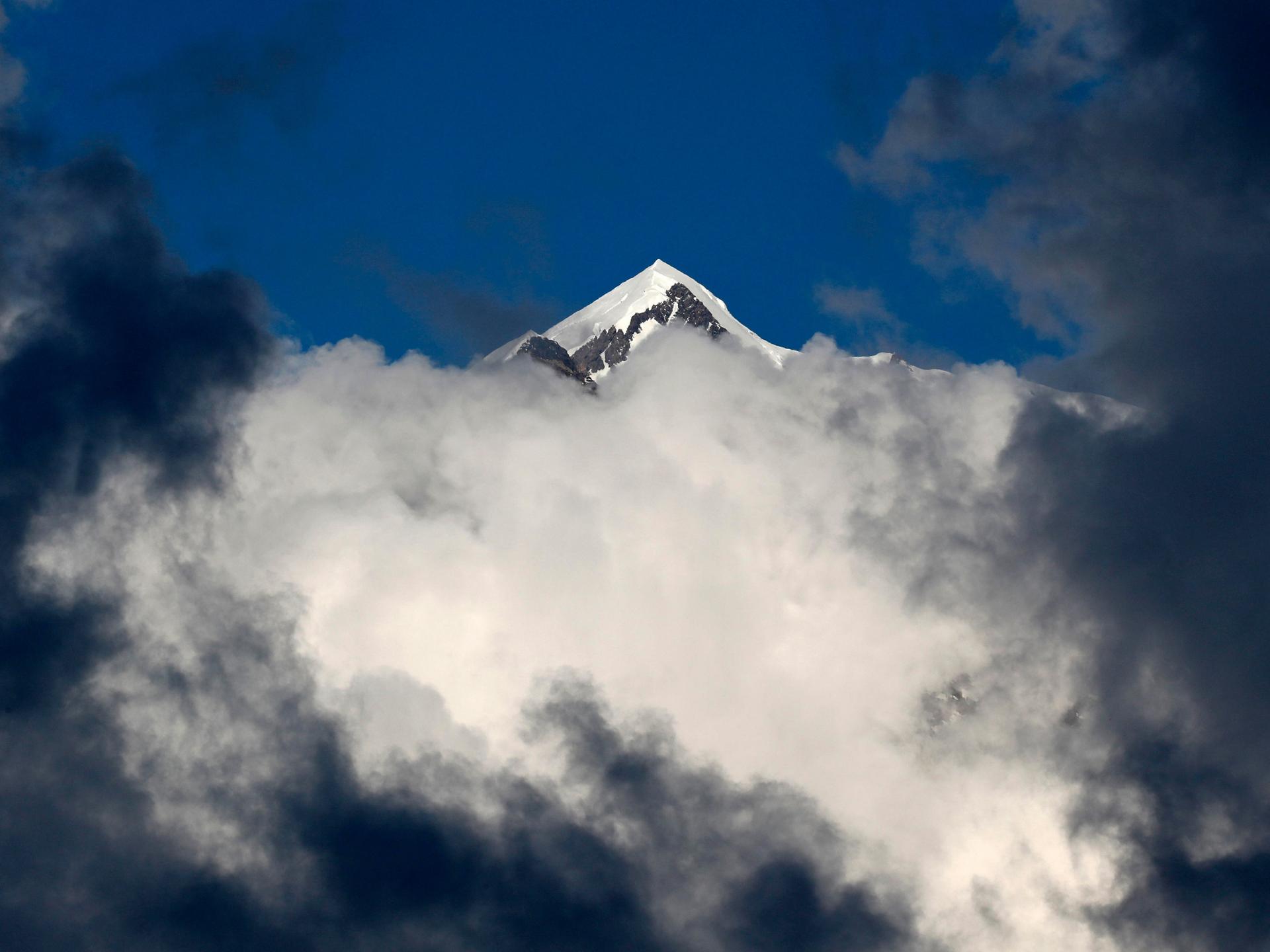 Eine verschneite Bergspitze des Mont-Blanc-Massivs ragt über grau-weiße Wolken in den tiefblauen Himmel empor.