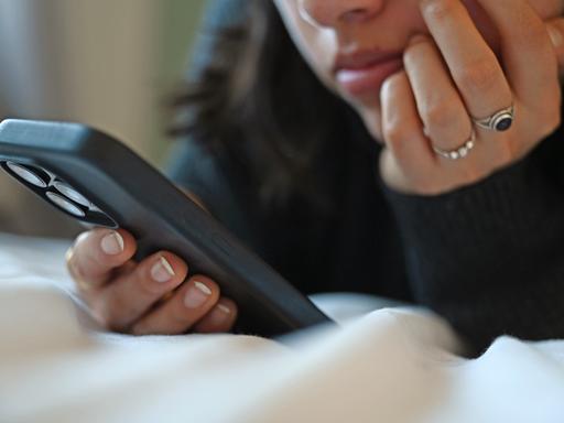 Eine junge Frau liegt mit dem Smartphone in der Hand auf dem Bett.