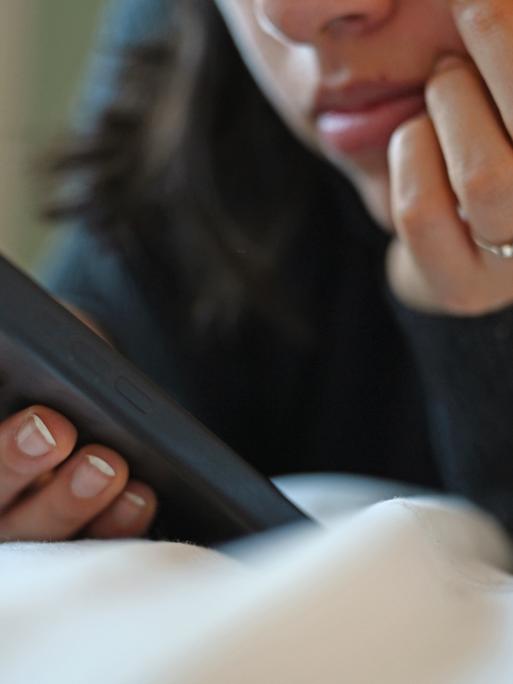 Eine junge Frau liegt mit dem Smartphone in der Hand auf dem Bett.