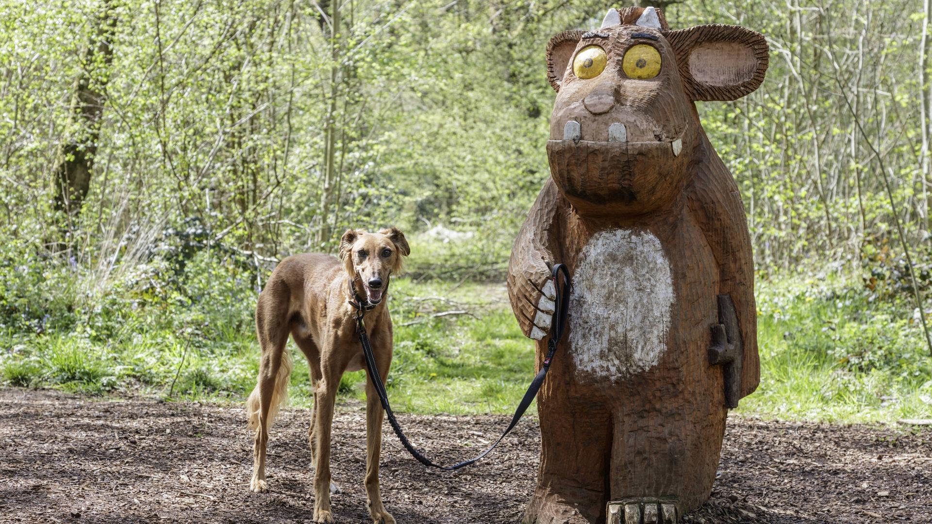 Eine Holzskulptur des Grüffelos steht im Wald und hält eienen Hund an der Leine. Eine Holzskulptur des Grüffelos steht im Wald und hält eienen Hund an der Leine.