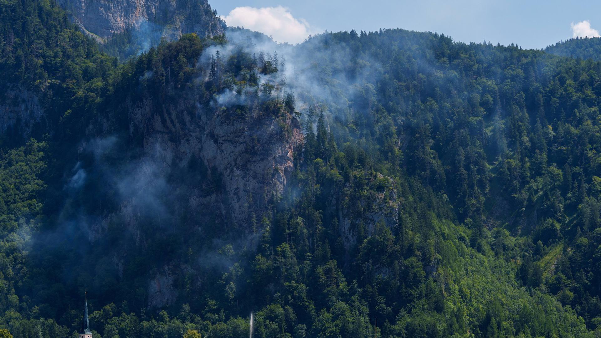 Flammen und Rauch sind in einem Waldstück an einem Berghang zu erkennen. Flammen und Rauch sind in einem Waldstück an einem Berghang zu erkennen.