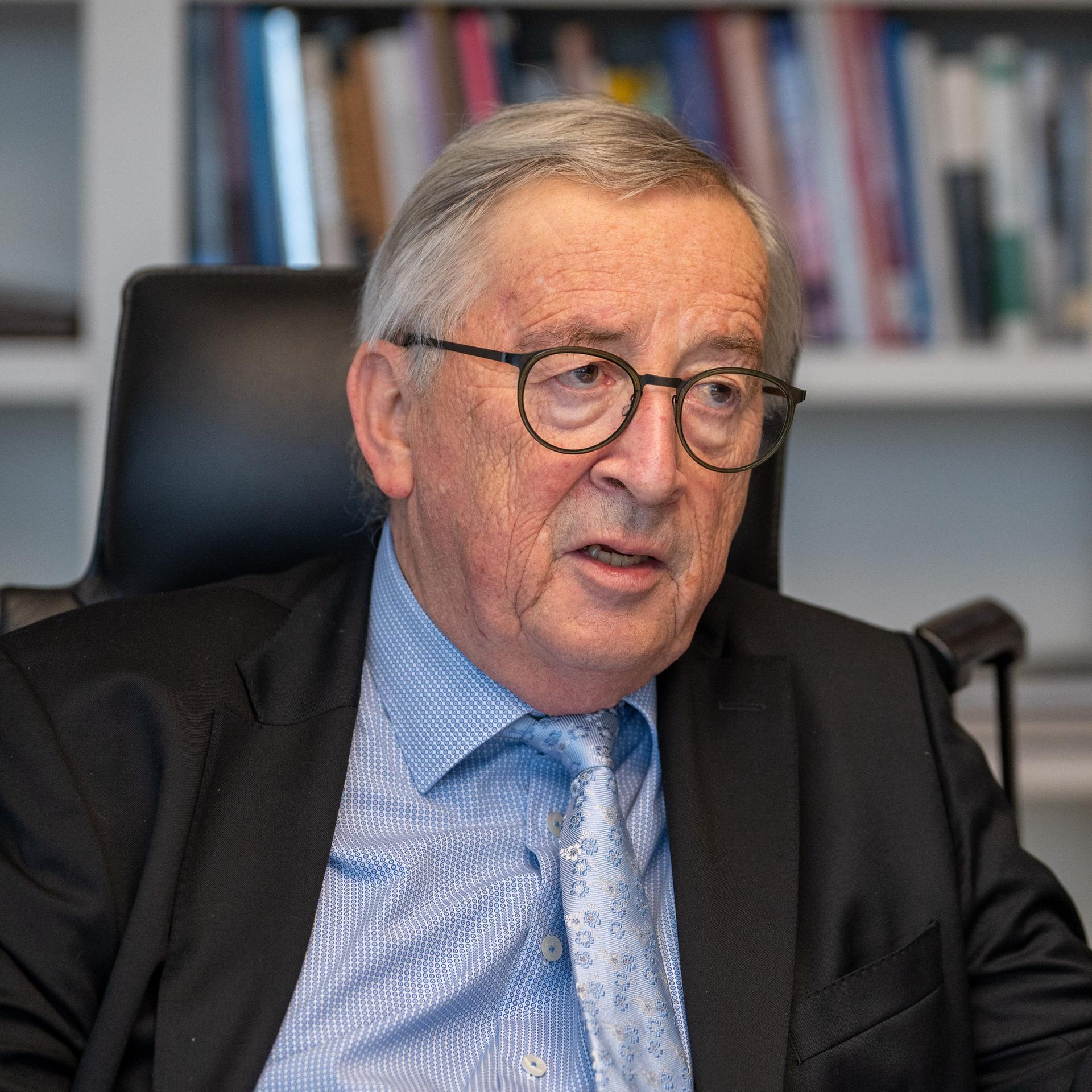 Jean-Claude Juncker, im Gespräch an seinem Schreibtisch, unterstreicht eine Aussage mit ausgestrecktem Zeigefinger.