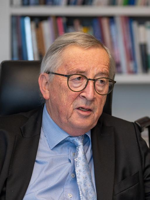 Jean-Claude Juncker, im Gespräch an seinem Schreibtisch, unterstreicht eine Aussage mit ausgestrecktem Zeigefinger.