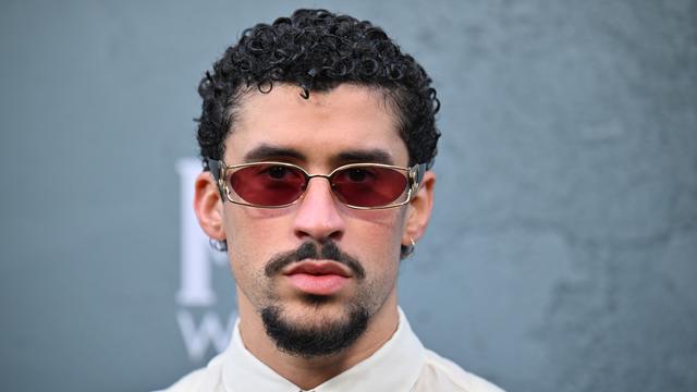 Ein Mann mit kurzen, schwarzen Locken. Er trägt eine Sonnen-Brille und ein weißes Hemd mit Krawatte.
