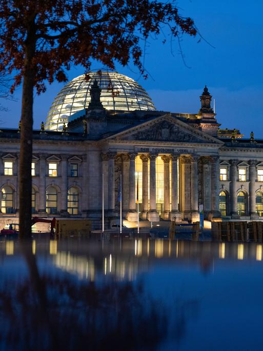 Die Reichstagskuppel in der Abenddämmerung. Es weht eine Deutschlandfahne vor dem blauen Himmel. 