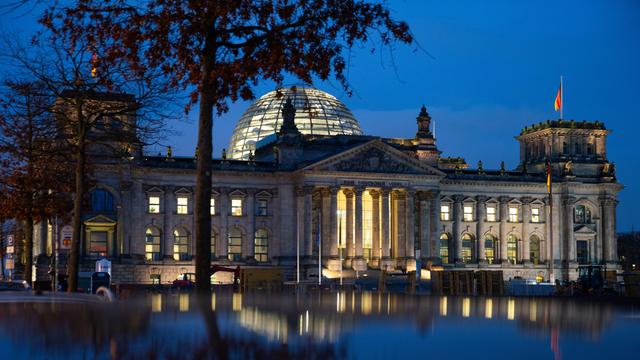 Die Reichstagskuppel in der Abenddämmerung. Es weht eine Deutschlandfahne vor dem blauen Himmel. 