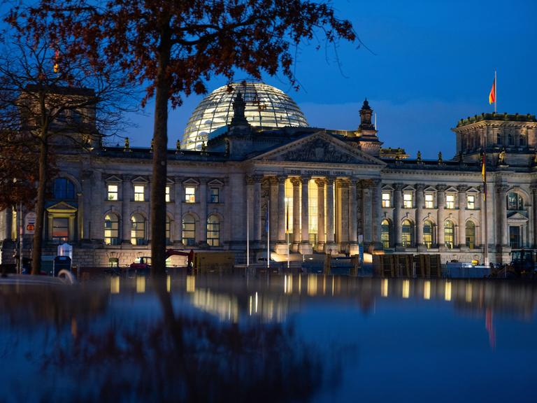 Die Reichstagskuppel in der Abenddämmerung. Es weht eine Deutschlandfahne vor dem blauen Himmel. 