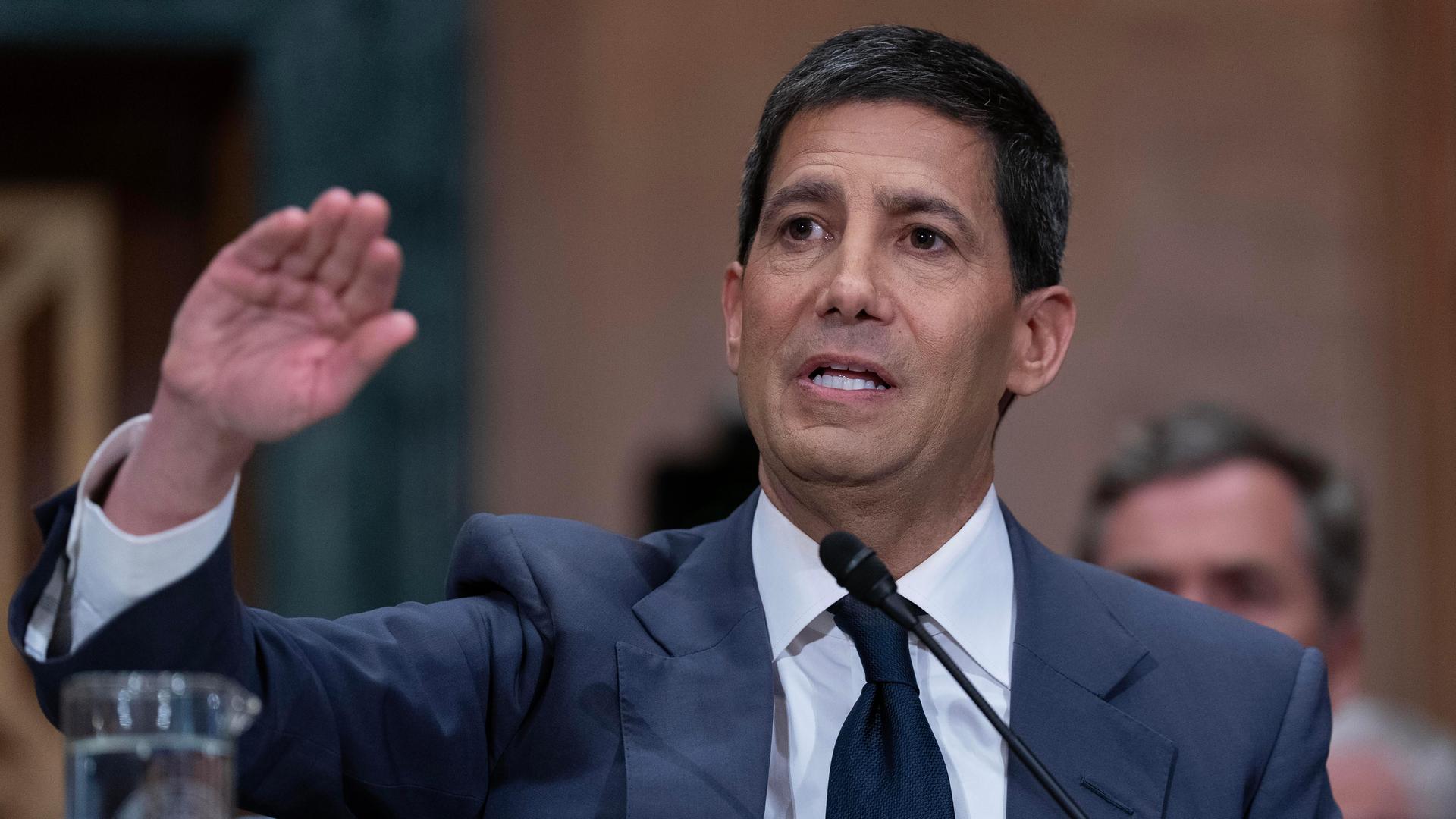 Kevin Warsh spricht vor dem Bankenausschuss des US-Senats. Er hat einen Arm leicht erhoben und spricht in ein Mikrofon.