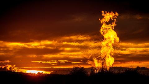 Eine Flamme schlägt vor glutrotem Abendhimmel auf einem Erdgasfeld in die Luft.