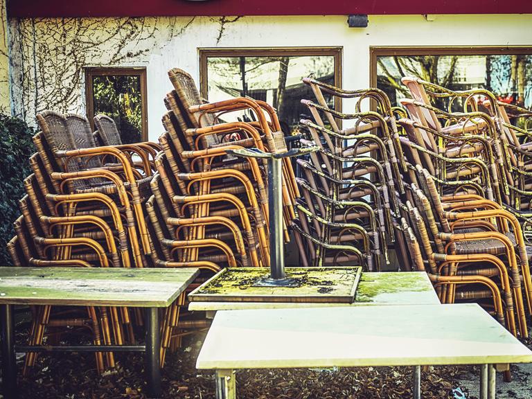 Gestapelte Stühle stehen draußen vor einem geschlossenen Restaurant.