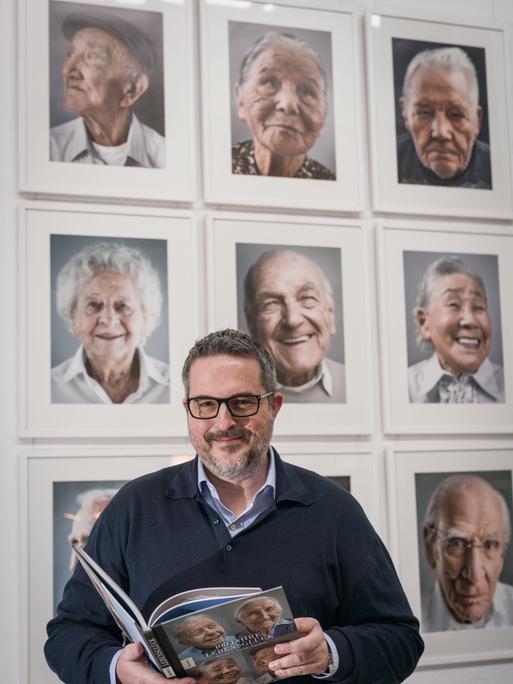 Der Fotograf Karsten Thormaehlen steht mit seinem Buch "Hundert Jahre Lebensglück" vor Fotos von Menschen, die das 100.Lebensjahr erreicht haben und die er porträtiert hat. 