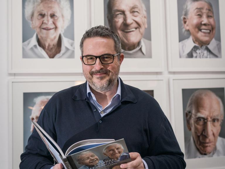 Der Fotograf Karsten Thormaehlen steht mit seinem Buch "Hundert Jahre Lebensglück" vor Fotos von Menschen, die das 100.Lebensjahr erreicht haben und die er porträtiert hat. 