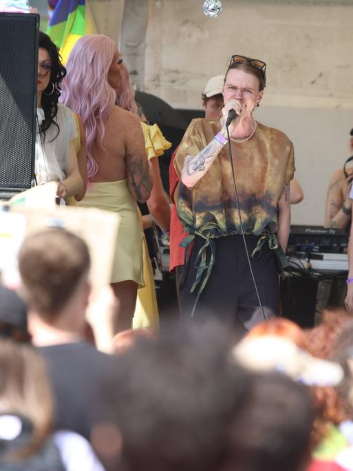 Luna Möbius steht auf der Bühne beim CSD in Leipzig und spricht am Mikrofon. Im Vordergrund steht das Publikum. Luna Möbius steht auf der Bühne beim CSD in Leipzig und spricht am Mikrofon. Im Vordergrund steht das Publikum.
