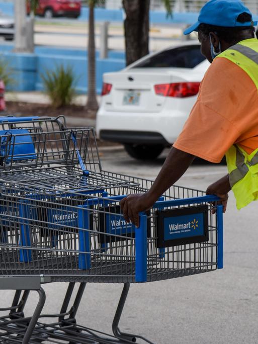 Ein Walmart-Mitarbeiter in Florida schiebt Einkaufswägen über einen Parkplatz.