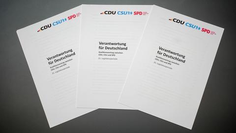 Drei Ausgaben des Koalitionsvertrages von CDU, CSU und SPD mit der Überschrift „Verantwortung für Deutschland“ liegen auf einem grauen Tisch.