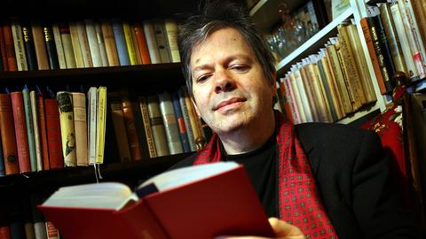 Der Verleger Thomas B. Schumann sitzt in seinem mit Büchern gefüllten Arbeitszimmer in Köln und blickt in ein Buch
