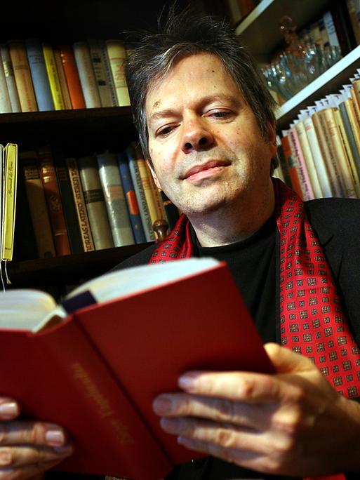 Der Verleger Thomas B. Schumann sitzt in seinem mit Büchern gefüllten Arbeitszimmer in Köln und blickt in ein Buch