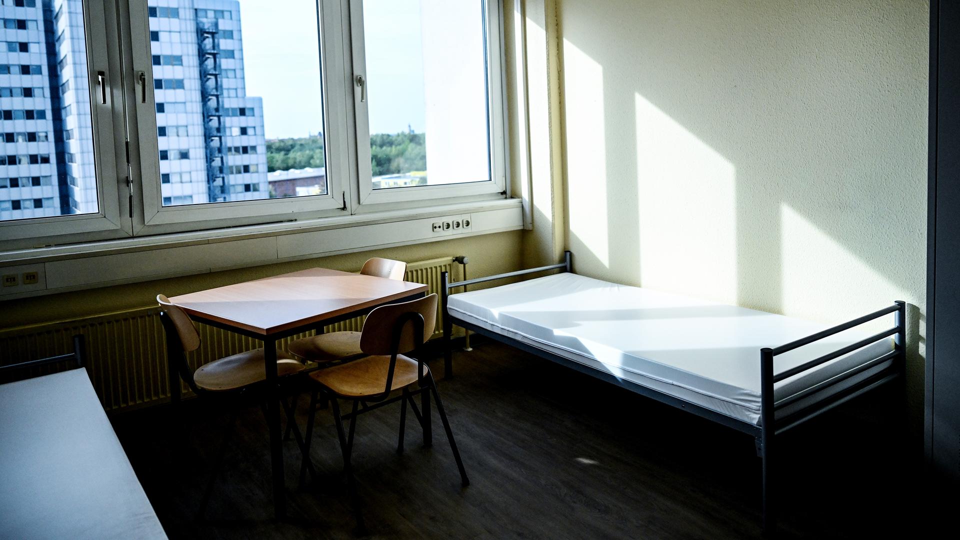 Blick in ein Zimmer in der Flüchtlingsunterkunft in Deutschland. Betten, ein Tisch, drei Stühle und ein Schrank stehen in einem Raum.