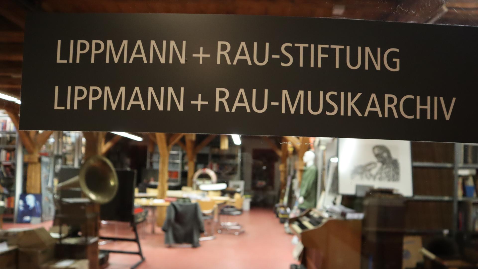 Blick in einen Raum, in dem im Vordergrund ein großes Schild prangt mit der Aufschrift "Lippmann und Rau-Stiftung" und "Lippmann und Rau-Musikarchiv". Im Hintergrund kann man schemenhaft eine Porträtradierung sehen und ein abgestelltes Grammophon.