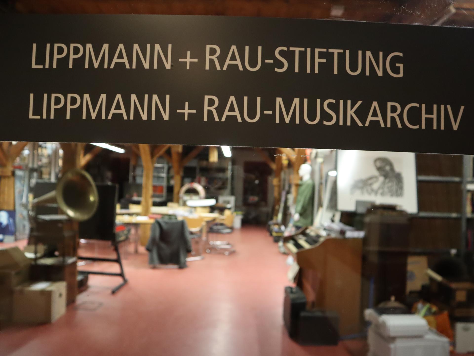 Blick in einen Raum, in dem im Vordergrund ein großes Schild prangt mit der Aufschrift "Lippmann und Rau-Stiftung" und "Lippmann und Rau-Musikarchiv". Im Hintergrund kann man schemenhaft eine Porträtradierung sehen und ein abgestelltes Grammophon.