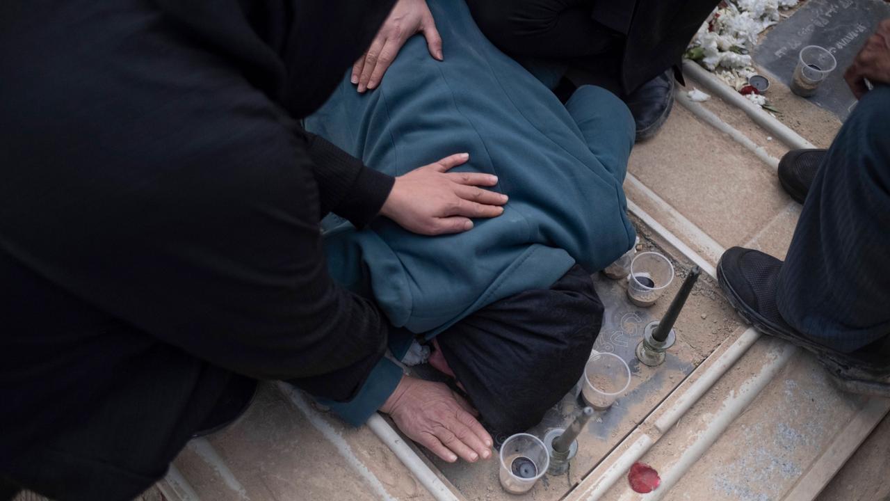 Trauernde Iraner auf einem Friedhof in Teheran. Eine Person beugt sich über ein Grab und ist von anderen Leuten umgeben.  