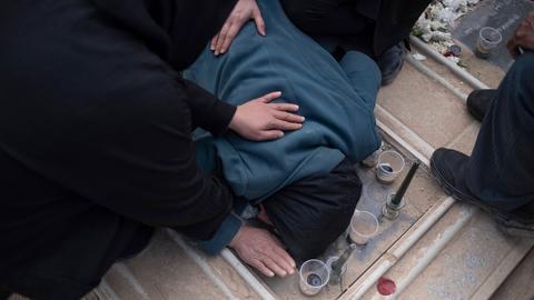 Trauernde Iraner auf einem Friedhof in Teheran. Eine Person beugt sich über ein Grab und ist von anderen Leuten umgeben.  