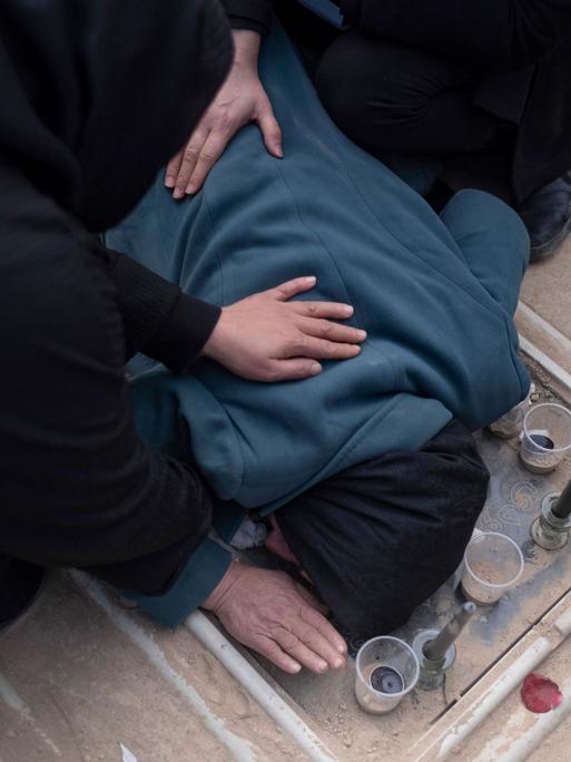 Trauernde Iraner auf einem Friedhof in Teheran. Eine Person beugt sich über ein Grab und ist von anderen Leuten umgeben. Trauernde Iraner auf einem Friedhof in Teheran. Eine Person beugt sich über ein Grab und ist von anderen Leuten umgeben.