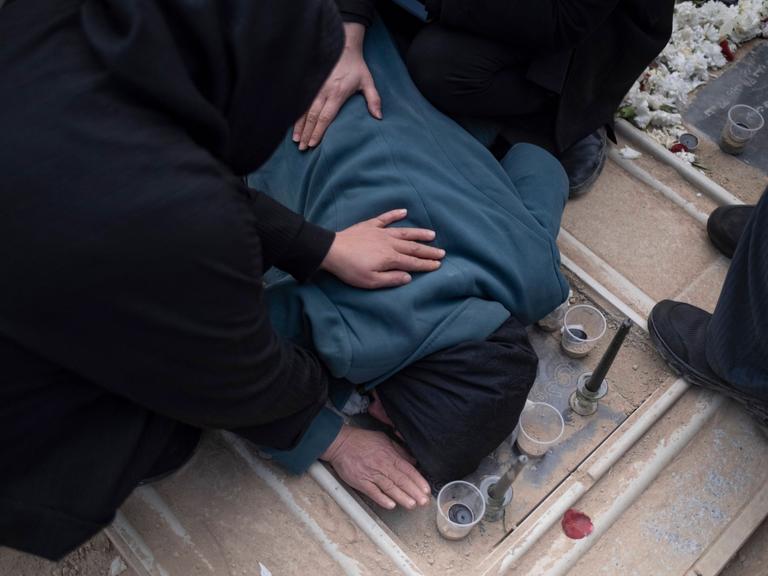 Trauernde Iraner auf einem Friedhof in Teheran. Eine Person beugt sich über ein Grab und ist von anderen Leuten umgeben.  