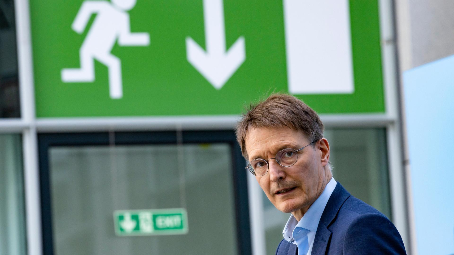 Gesundheitsminister Karl Lauterbach blickt Richtung Kamera, er steht unter einem grünen Notausgang-Schild