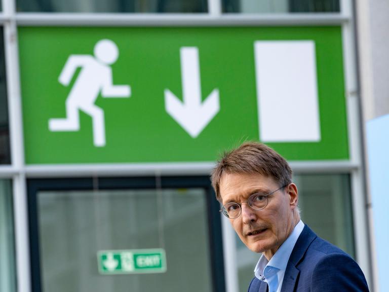 Gesundheitsminister Karl Lauterbach blickt Richtung Kamera, er steht unter einem grünen Notausgang-Schild
