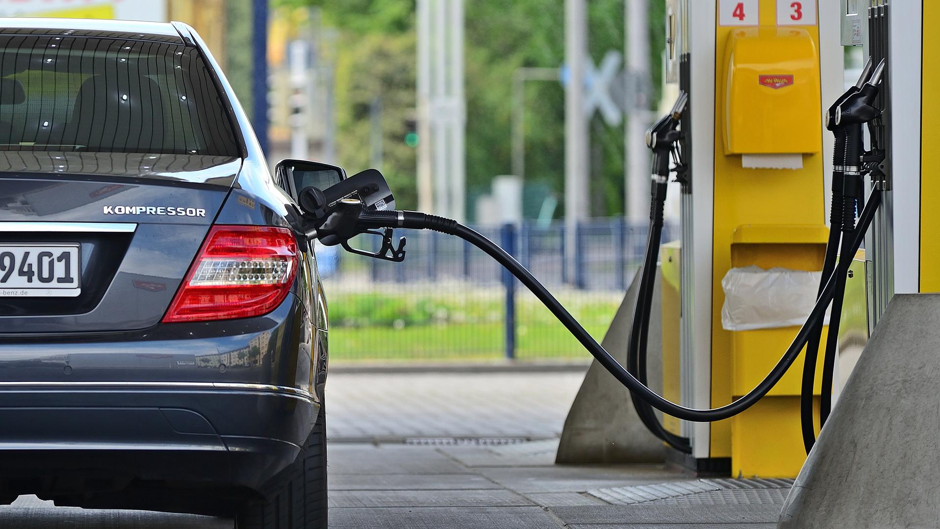 Ein Benzinzapfhahn steckt in einer grauen Mercedes-Limousine, die an einer Tankstelle steht.