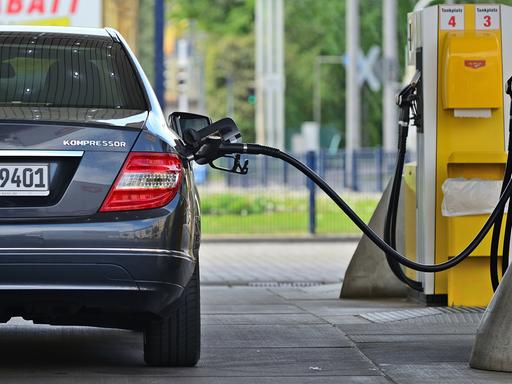 Ein Benzinzapfhahn steckt in einer grauen Mercedes-Limousine, die an einer Tankstelle steht. Ein Benzinzapfhahn steckt in einer grauen Mercedes-Limousine, die an einer Tankstelle steht.