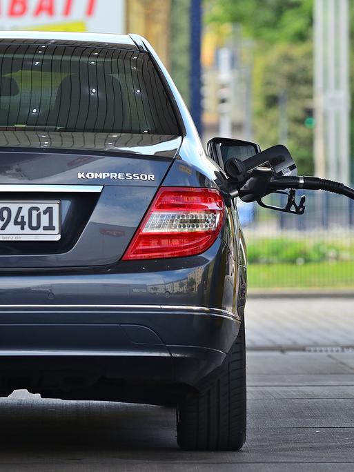 Ein Benzinzapfhahn steckt in einer grauen Mercedes-Limousine, die an einer Tankstelle steht. Ein Benzinzapfhahn steckt in einer grauen Mercedes-Limousine, die an einer Tankstelle steht.