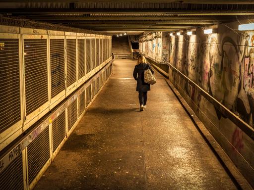 Eine Frau geht abends allein durch eine Unterführung.