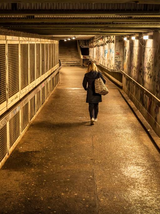 Eine Frau geht abends allein durch eine Unterführung.