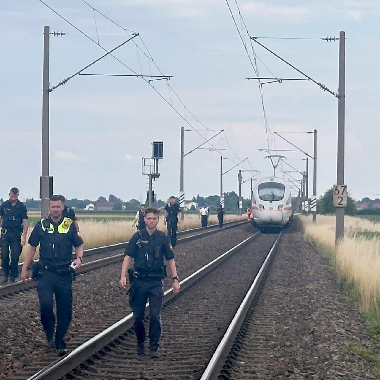 Straßkirchen: Polizeibeamte gehen vor einem ICE, in dem ein Mann in Niederbayern mehrere Passagiere angegriffen hat, durch das Gleisbett. 