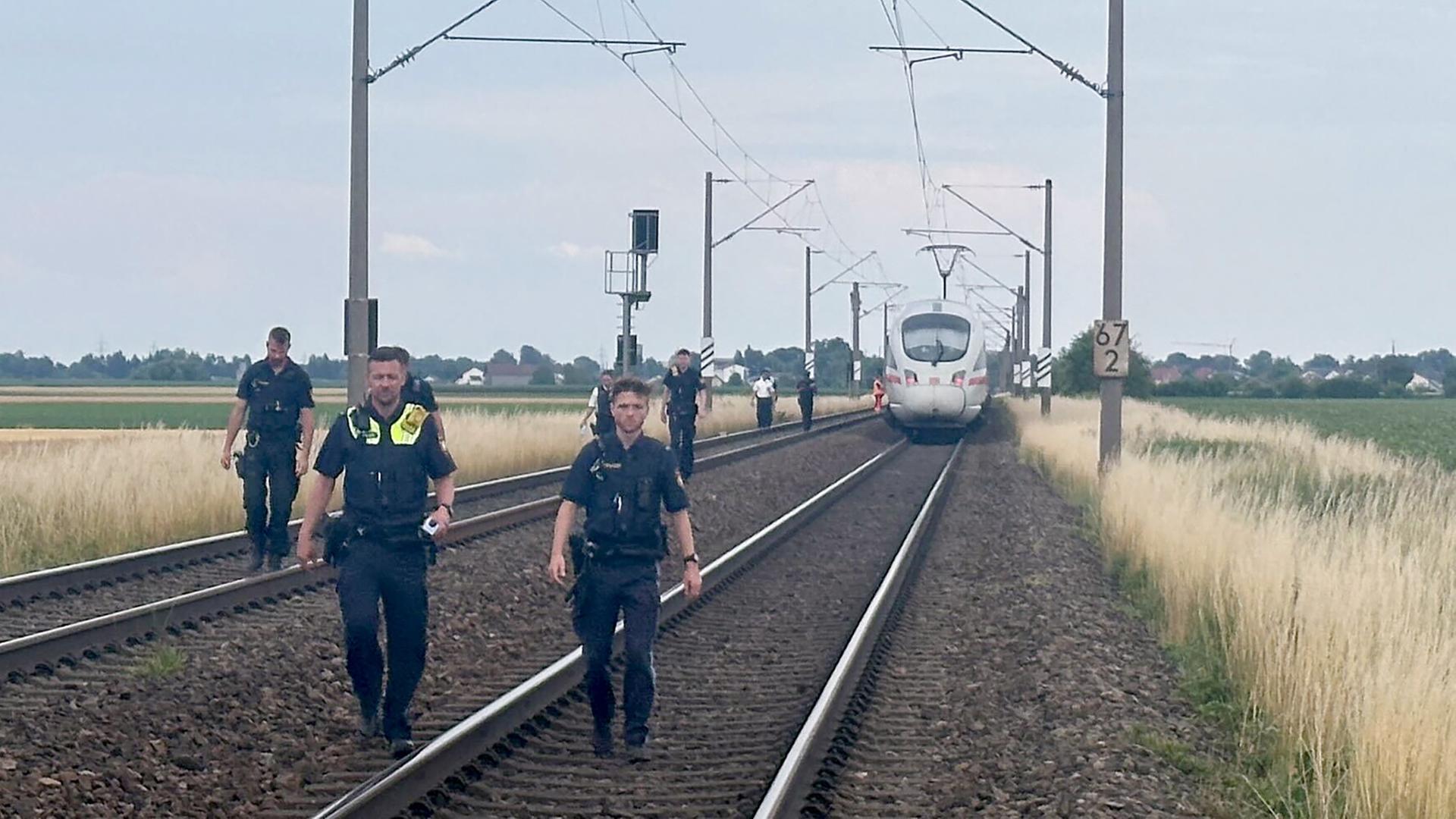 Straßkirchen: Polizeibeamte gehen vor einem ICE, in dem ein Mann in Niederbayern mehrere Passagiere angegriffen hat, durch das Gleisbett. 