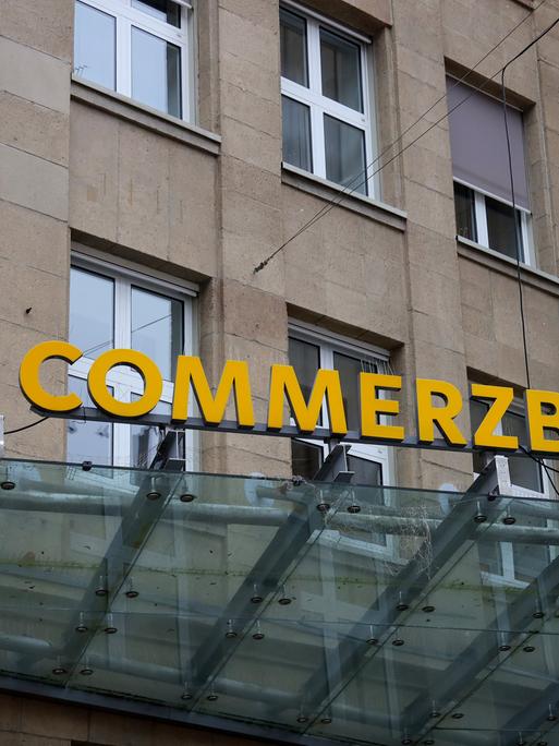 Das Eingangsportal einer Commerzbankfiliale mit dem Schriftzug "Commerzbank" in einem steinernen Gebäude.