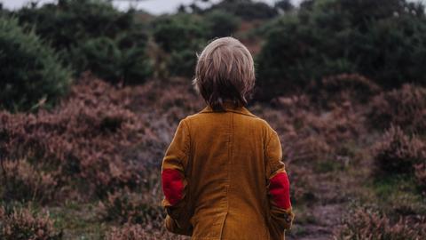 Wir sehen den Rücken eines Jungen, der durch die Natur läuft.
