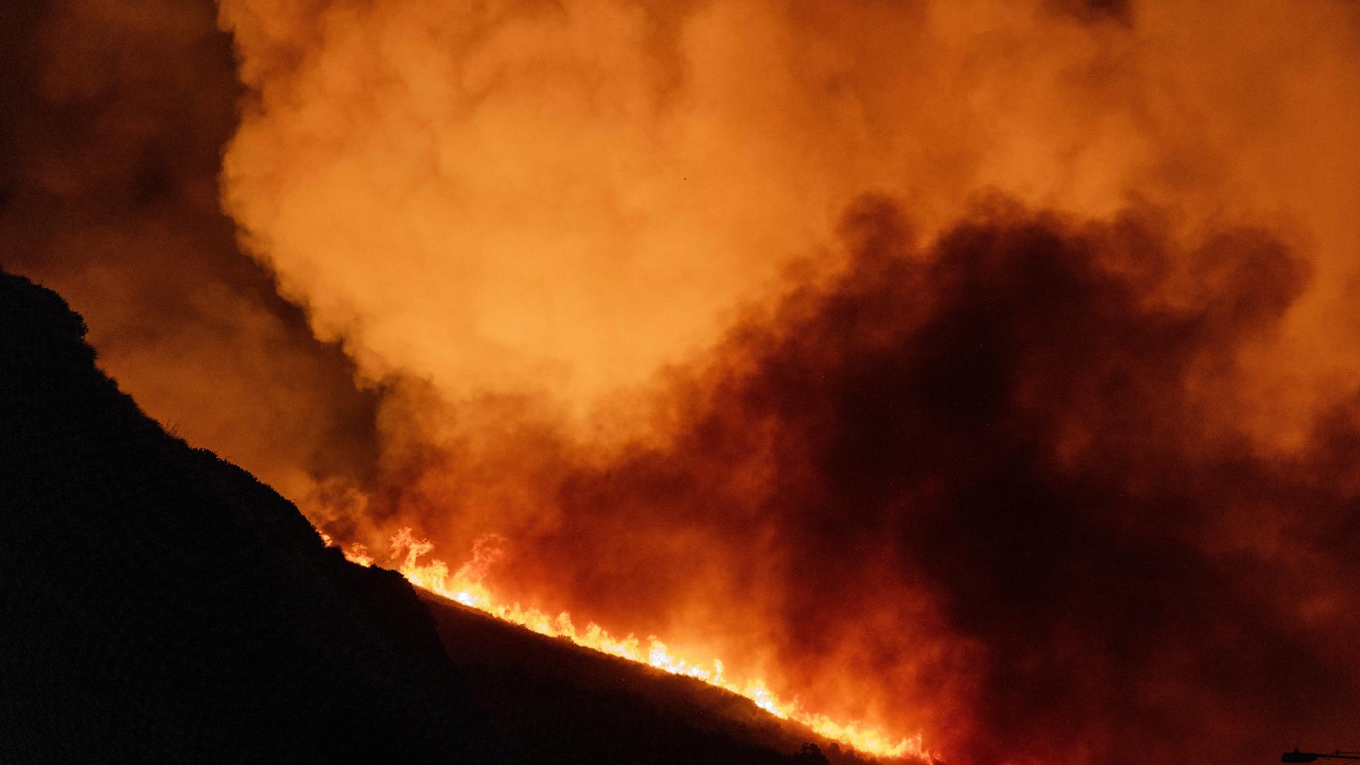 Auf einem Berg wütet ein Feuer mit heftiger Rauchbildung. Man sieht nur die Umrisse des Hügels. 