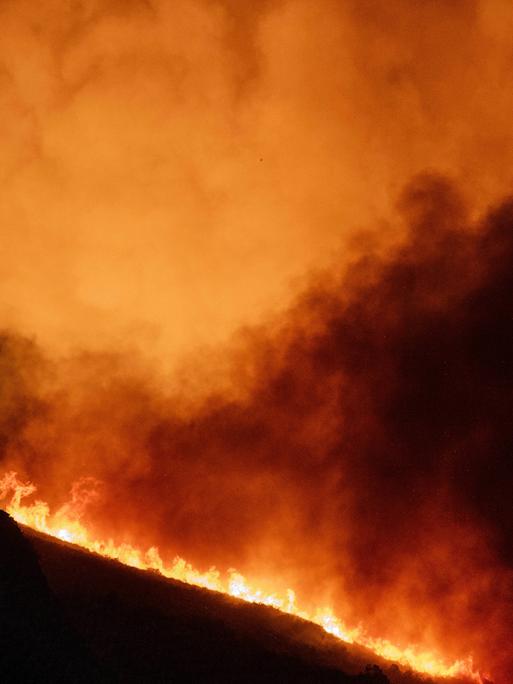 Auf einem Berg wütet ein Feuer mit heftiger Rauchbildung. Man sieht nur die Umrisse des Hügels. 