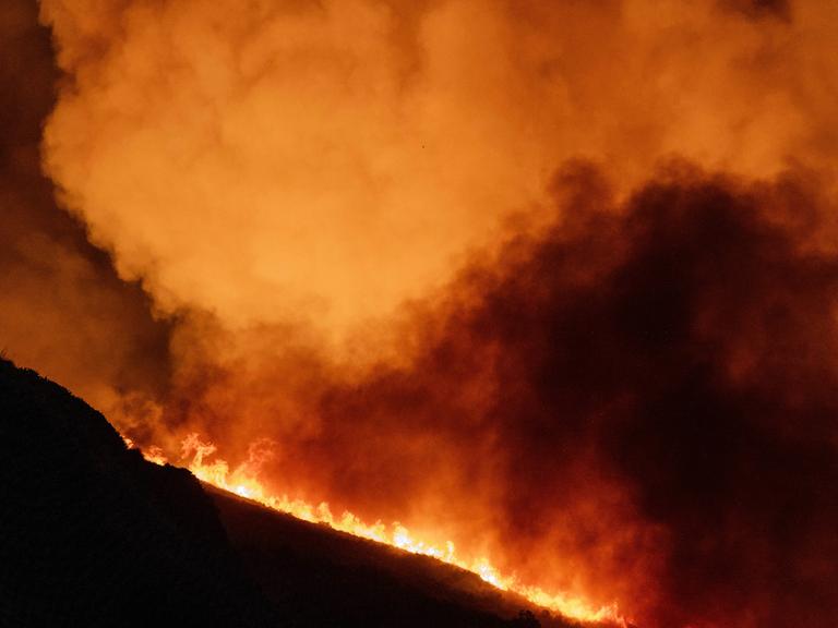 Auf einem Berg wütet ein Feuer mit heftiger Rauchbildung. Man sieht nur die Umrisse des Hügels. 