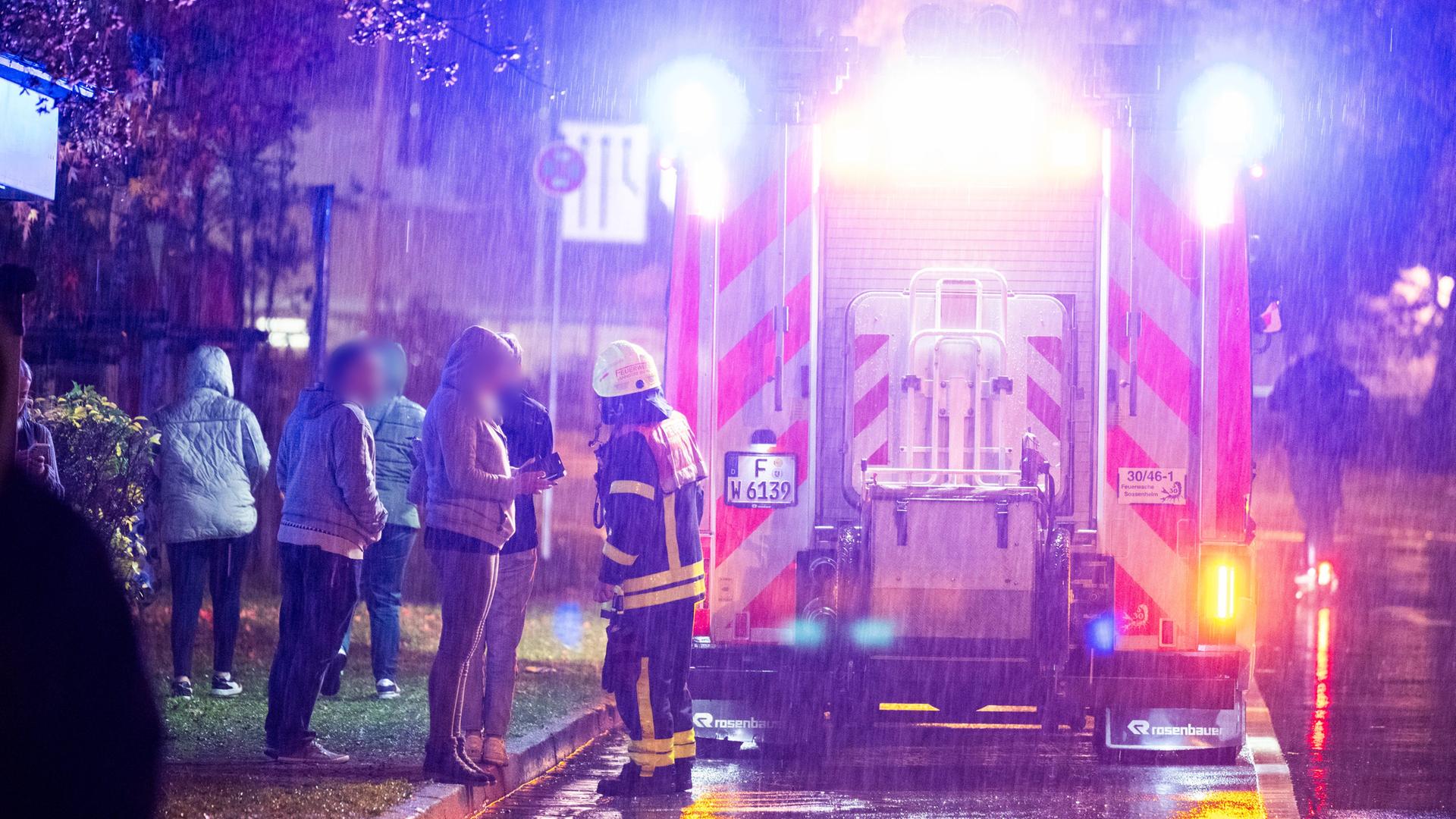 Menschen stehen neben einem Krankenwagen am Nordwestzentrum in Frankfurt und sprechen mit einer Einsatzkraft der Feuerwehr. Menschen stehen neben einem Krankenwagen am Nordwestzentrum in Frankfurt und sprechen mit einer Einsatzkraft der Feuerwehr.